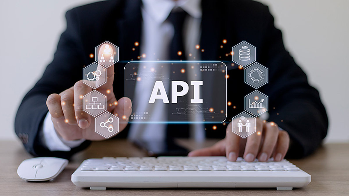 A person in a business suit touching a glowing API icon surrounded by data, workflow and sharing symbols above a keyboard