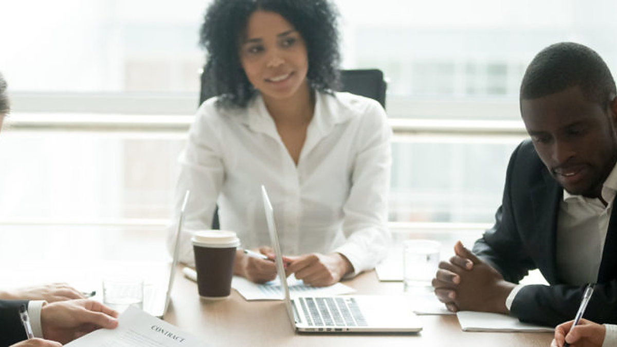 Colleagues seated around a conference table with laptops, reviewing a document together in a meeting