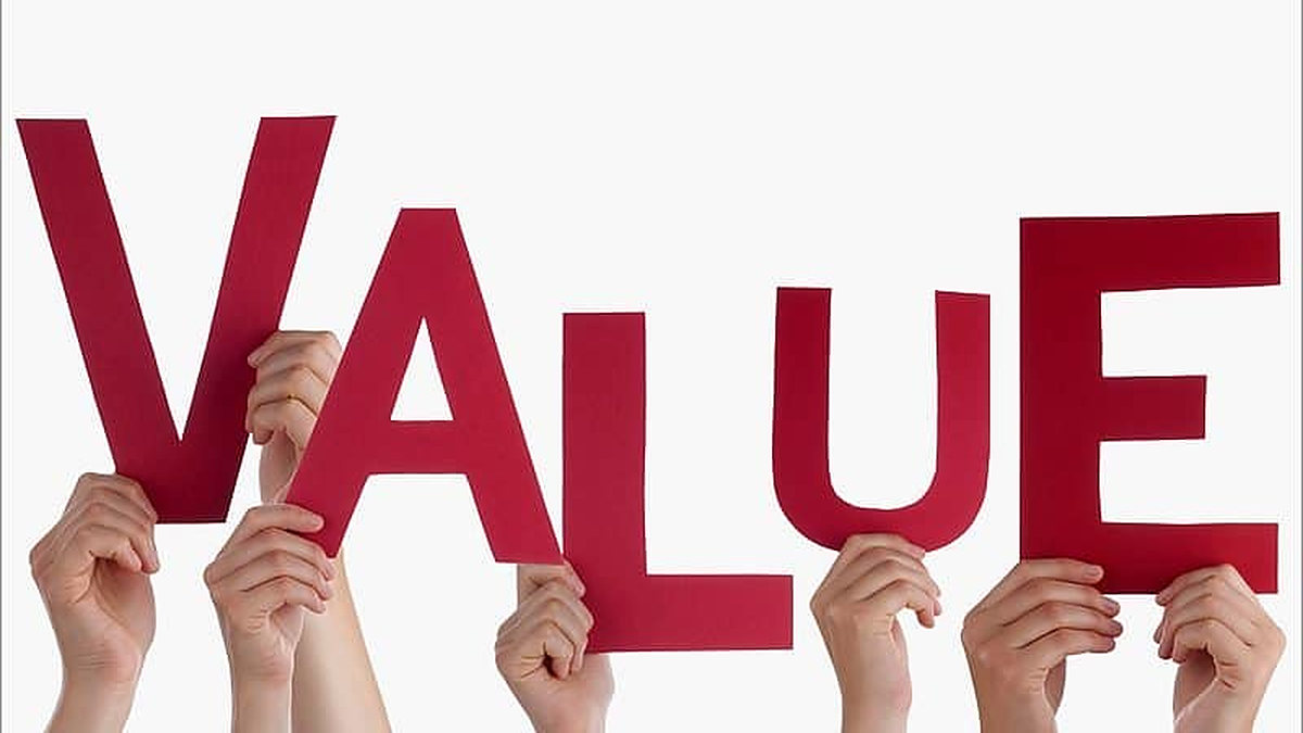 Hands holding up large red cardboard letters that spell VALUE